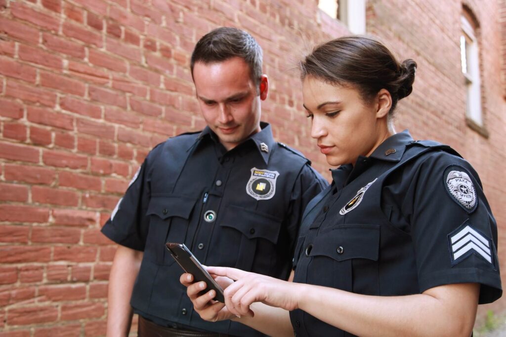 Two AF Patrol security guards in uniform reviewing information on a mobile device in an alleyway.